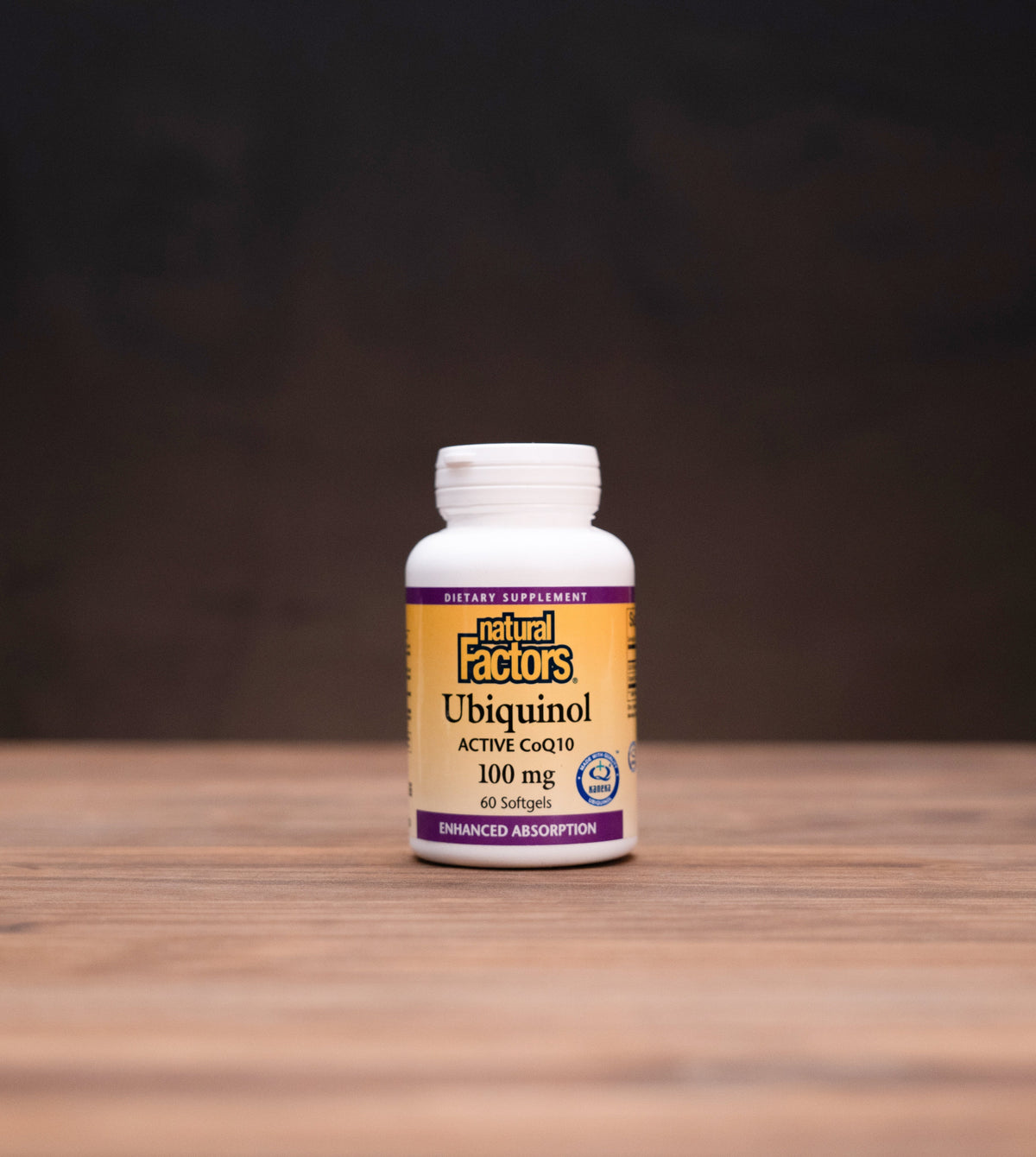 A bottle of Natural Ecos Ubiquinol 100 mg dietary supplement standing on a wooden surface against a dark background, with small mystical props visible on both sides.