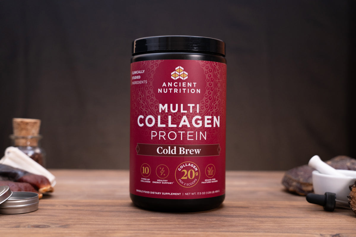 A jar of Ancient Nutrition Multi Collagen Protein in the Cold Brew flavor, displayed on a wooden surface with a dark, moody background and small rustic props.