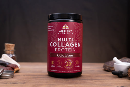 A jar of Ancient Nutrition Multi Collagen Protein in the Cold Brew flavor, displayed on a wooden surface with a dark, moody background and small rustic props.