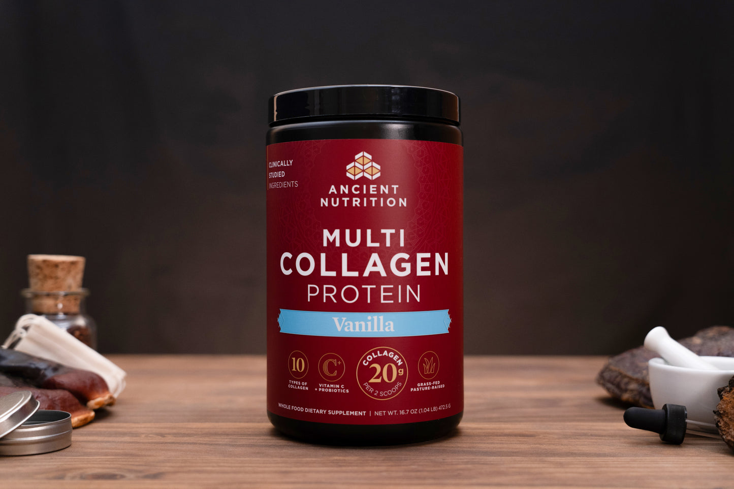 A jar of Ancient Nutrition Multi Collagen Protein in Vanilla flavor, set on a wooden table with a dark background and small decorative props on either side.