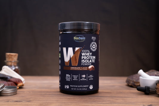 A jar of Biochem Nutrition Whey Protein Isolate in chocolate flavor, displayed on a wooden surface with a dark background and small kitchen props.
