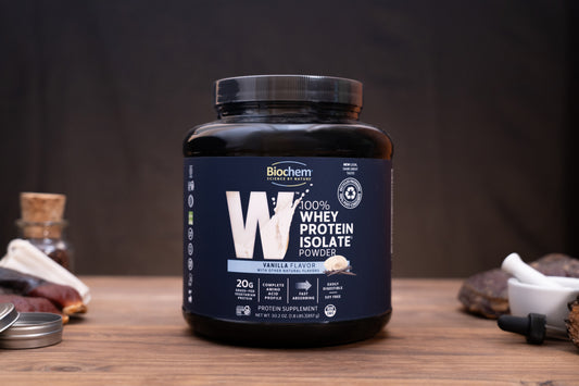 Biochem Nutrition Vanilla Flavor Whey Protein Isolate Powder in a black tub with a dark navy label, displayed on a wooden surface with small kitchen props.