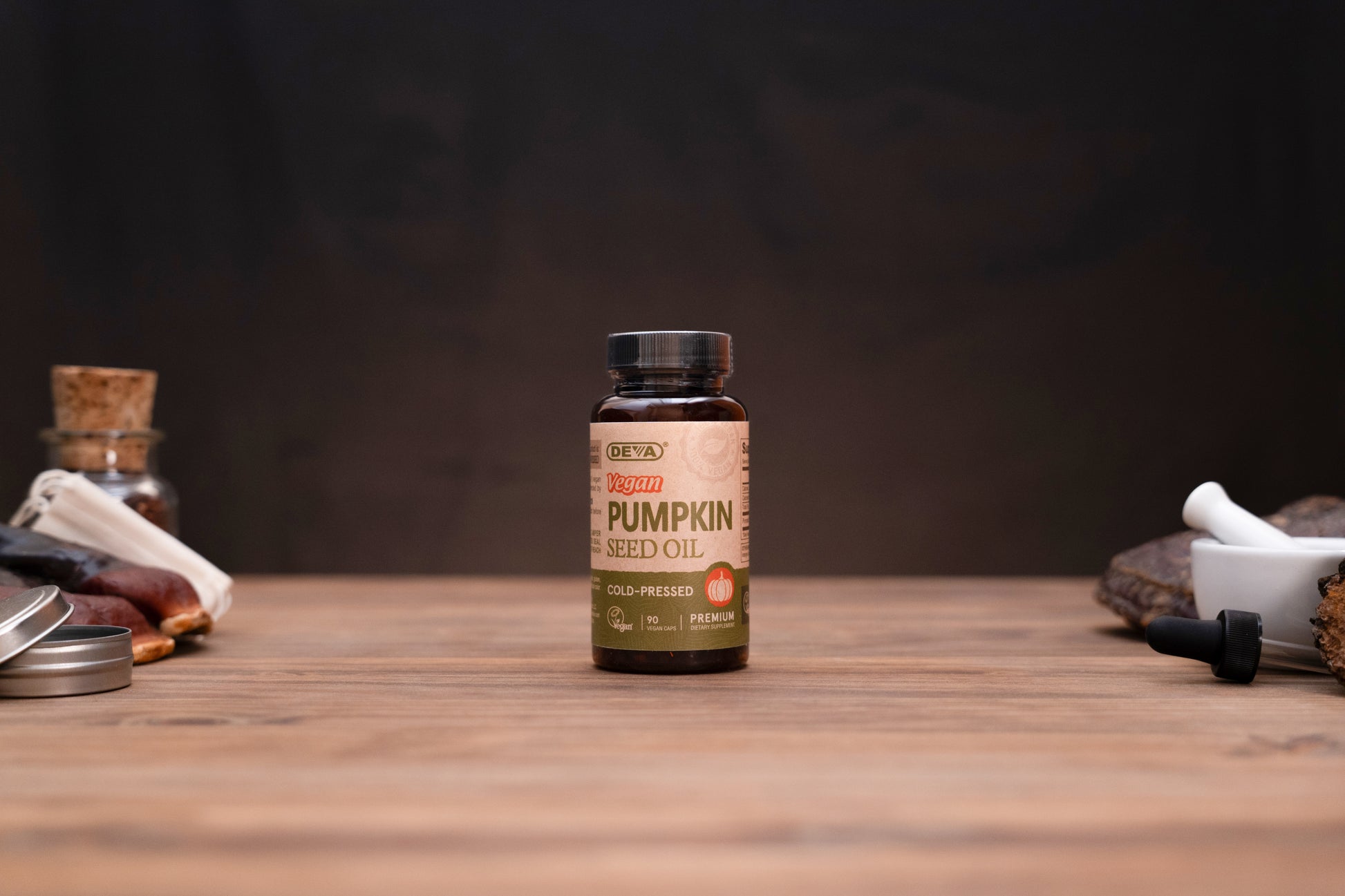 A bottle of ORKS Organic Pumpkin Seed Oil centered on a wooden tabletop with a dark, moody background. The amber glass bottle has a black cap and a tan label with green and orange text.
