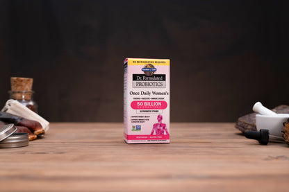 A box of Dr. Svarup's Probiotics Once Daily Women's 50 Billion CFUs stands centered on a wooden tabletop, flanked by blurred herbal and apothecary props against a dark background.
