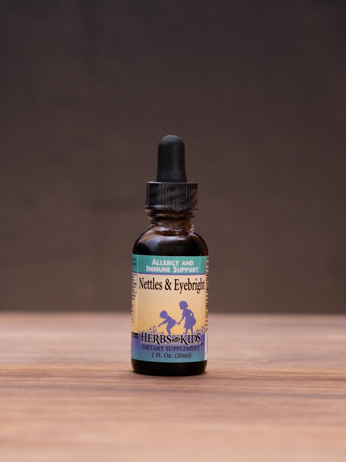 A small amber glass dropper bottle with a cream label stands centered on a wooden tabletop against a dark brown backdrop. The label reads 'Saffron & Turmeric' with a blue horse illustration.