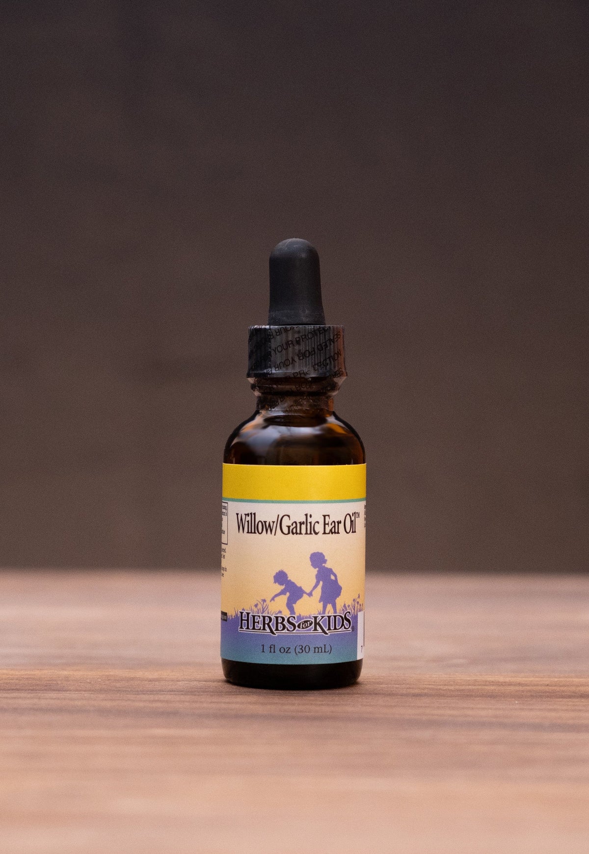 A small amber glass dropper bottle with a black cap stands centered on a wooden surface against a dark backdrop. The bottle has a cream label with blue and purple graphics and the text 'Mucosal Immunity'.