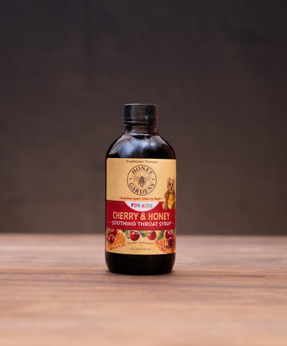 A bottle of Honey Creek Vanilla Extract centered on a wooden table, with rustic ingredients and tools softly blurred in the background and foreground.