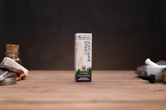 A box of Mountain Organic Lion's Mane Extract stands on a wooden tabletop against a dark background, with small herbal-themed props visible on both sides.