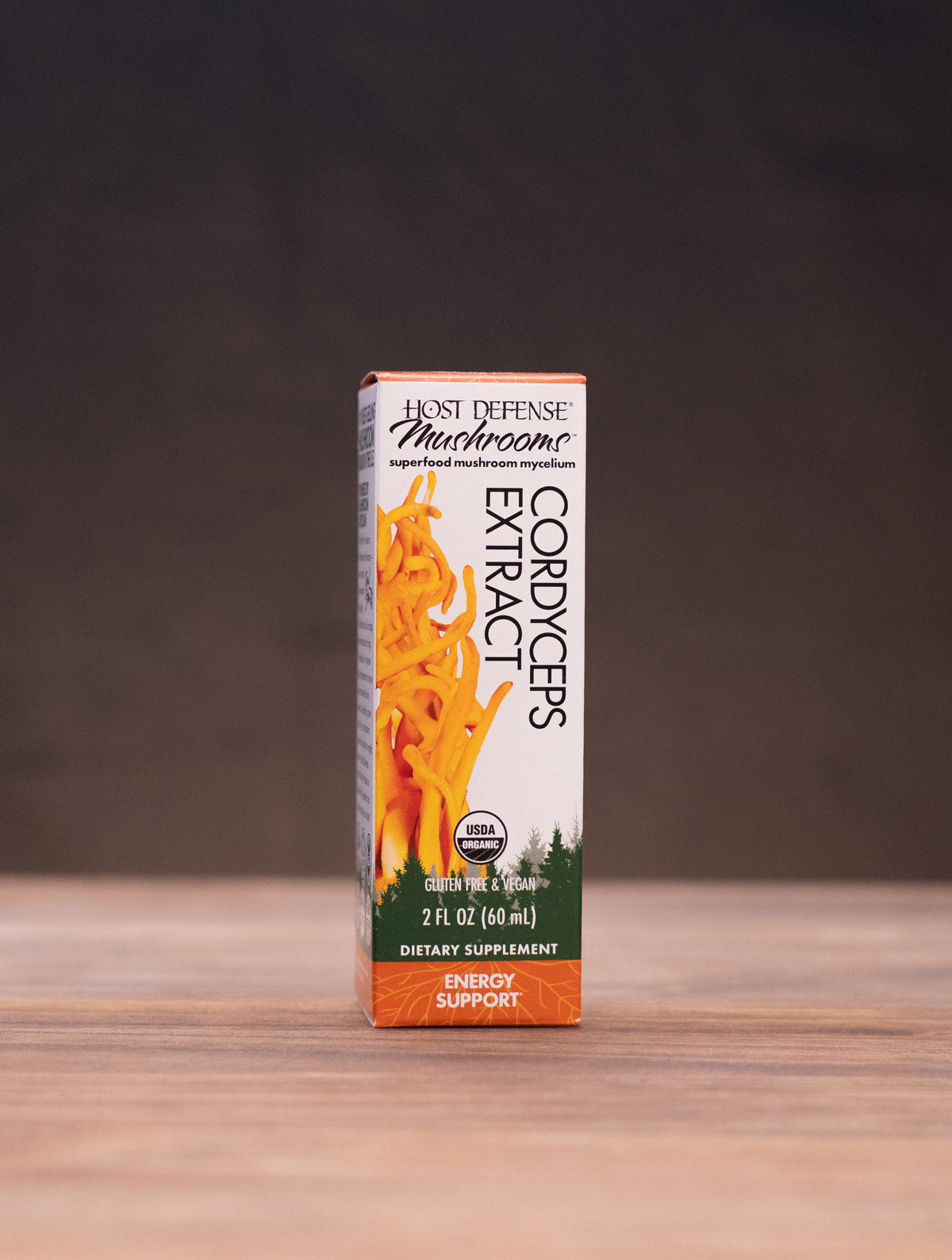 A box of Mushroom Gummies by Wild Mushroom Company stands centered on a wooden tabletop, with blurred rustic props on both sides against a dark background.
