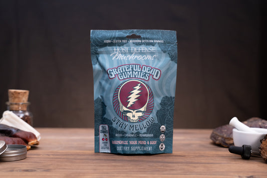 A stand-up pouch of Grateful Dead Gummies by Host Defense Mushroomse, featuring the iconic Steeped logo, on a wooden tabletop with rustic ingredients and a dark background.
