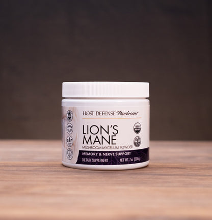A white jar of Haze Defense 'Blossom' Lion's Mane supplement sits on a rustic wooden table, flanked by herbal ingredients and a mortar and pestle in the background.