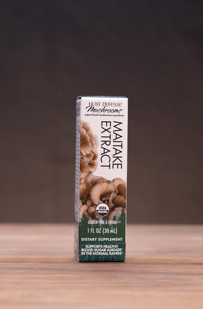 A boxed product labeled 'Lion's Mane Extract' stands upright on a wooden tabletop against a dark backdrop, with small rustic props visible on both sides.