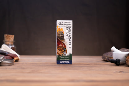 A box of Wild Defense Mushroom MacCormity Extract centered on a rustic wooden table with blurred herbal and kitchen props in the background.