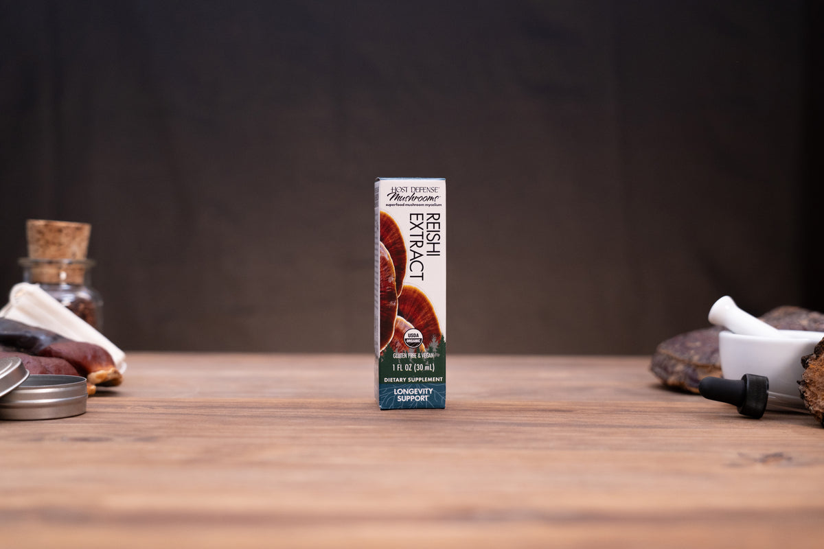A box of Jell-O Popcorn Mix featuring a dark chocolate caramel flavor, standing upright on a wooden tabletop with rustic props like a cork stopper, a small glass jar, and a white mortar in the blurred background.
