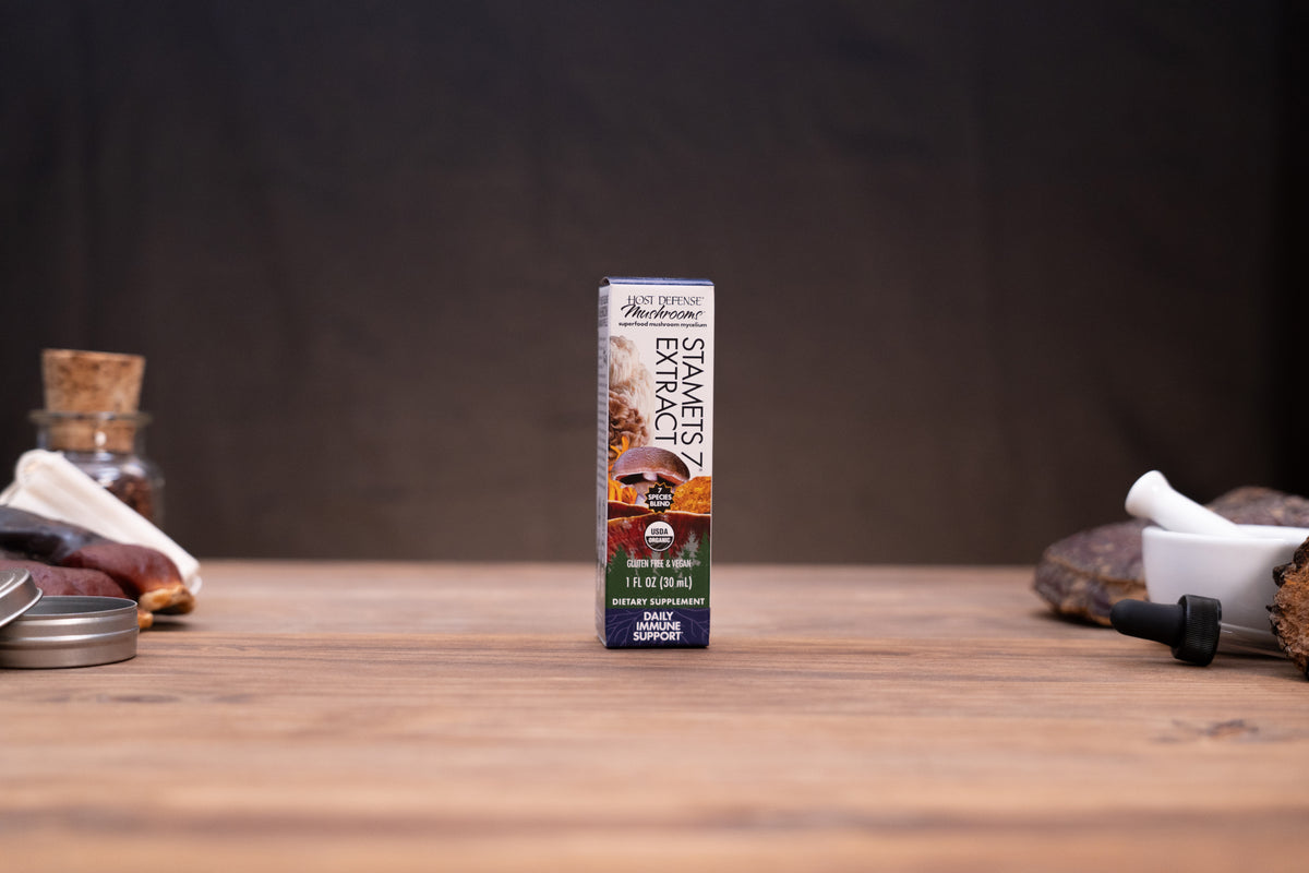 A small boxed product labeled 'Smoked Extract' stands upright on a wooden tabletop against a dark backdrop, with blurred rustic props on both sides.