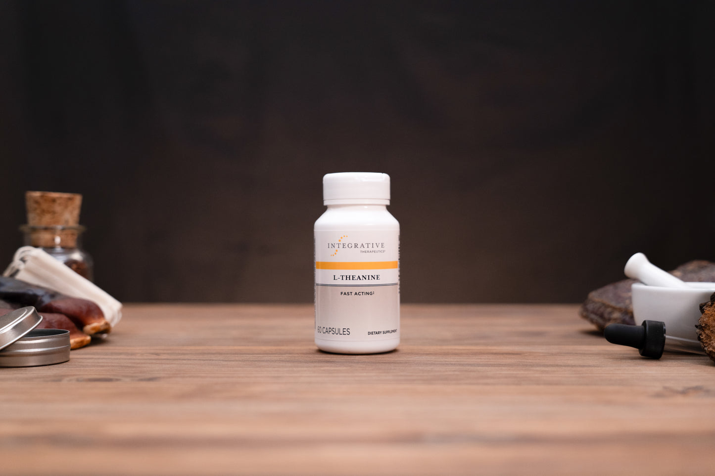 A white bottle of Integrative Medicine Lithospermum capsules stands centered on a wooden tabletop against a dark background, with blurred herbal props on both sides.