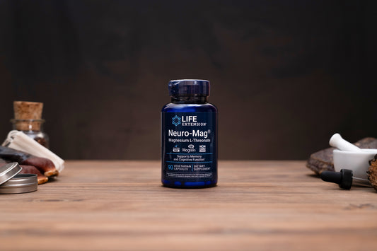 A dark blue bottle of Life Extension Neuro-Mag Magnesium L-Threonate supplement, centered on a wooden tabletop with blurred herbal and laboratory props in the background.