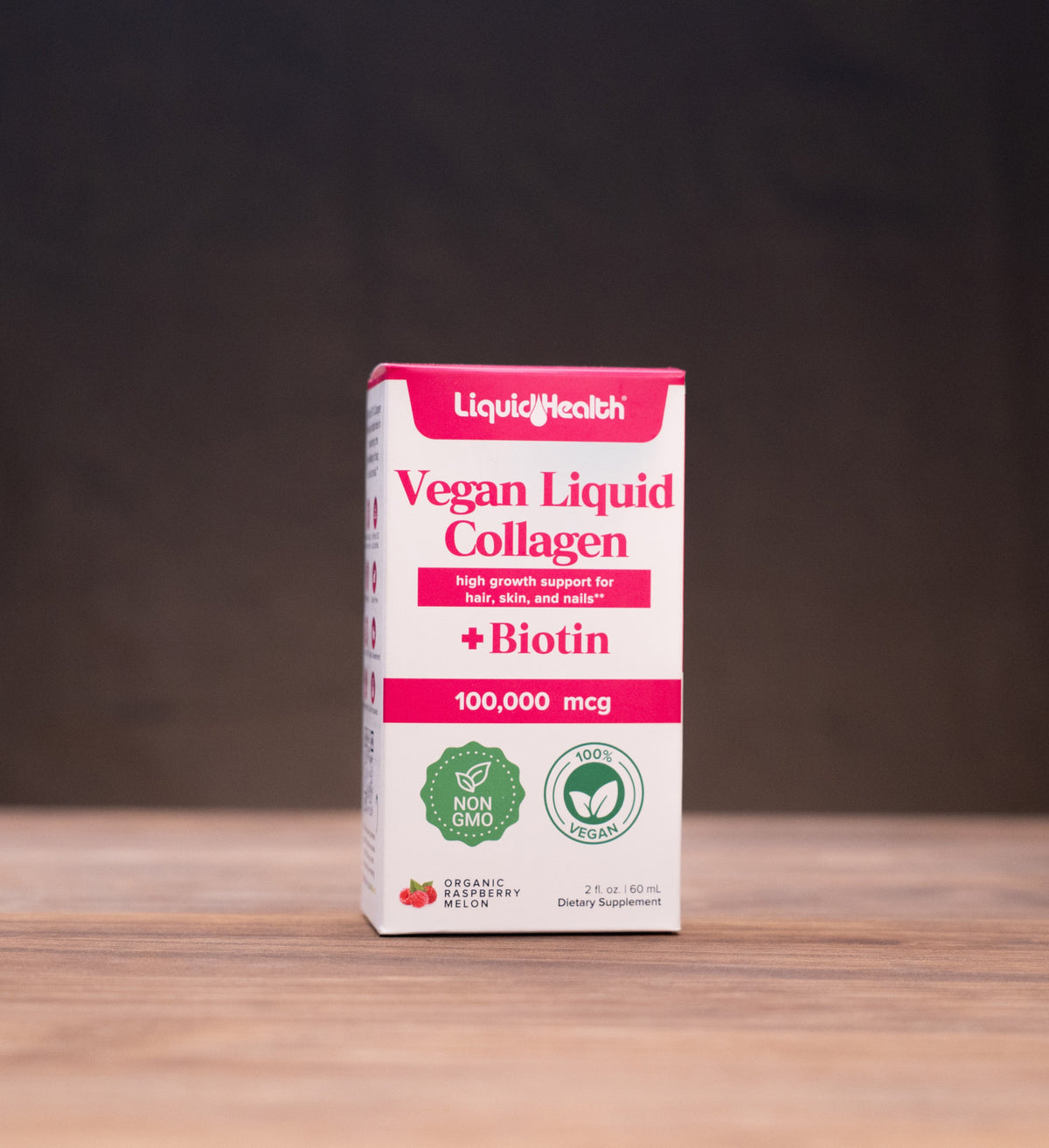 A box of LiquidHealth Vegan Liquid Collagen with Biotin, 100,000 mcg, standing on a wooden table with rustic props in the background.
