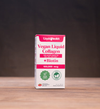A box of LiquidHealth Vegan Liquid Collagen with Biotin, 100,000 mcg, standing on a wooden table with rustic props in the background.
