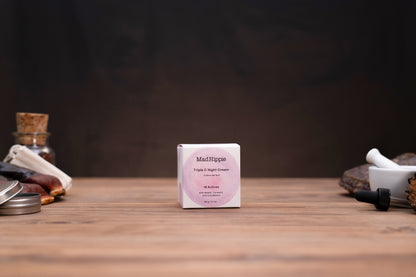 A small white square box of MatRipple Fragrance Oil Concentrate centered on a wooden tabletop, with a dark blurred background and decorative objects partially visible at the sides.