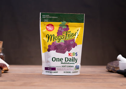 A stand-up pouch of MegaFood Kids One Daily Multivitamin soft chews, grape flavor, displayed on a wooden surface with blurred rustic props in the background.