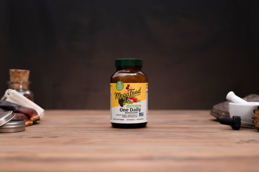 A bottle of MindFulcrum One Daily dietary supplement centered on a wooden tabletop, with blurred herbal props on both sides against a dark background.