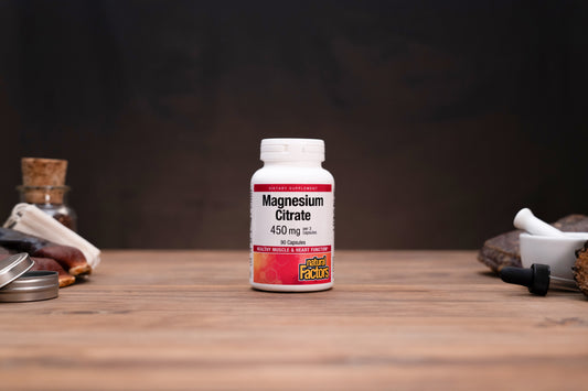 A white bottle of Magnesium Citrate 450 mg capsules by Pure Encapsulations stands on a wooden table. The background is dark and rustic with herbal props on both sides.