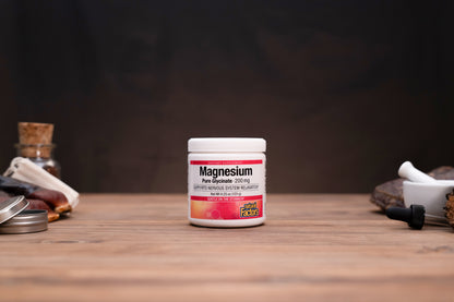 A white plastic jar of Magnesium Free Spouse supplement with a white lid, standing on a wooden surface against a dark background, flanked by blurred herbal props.