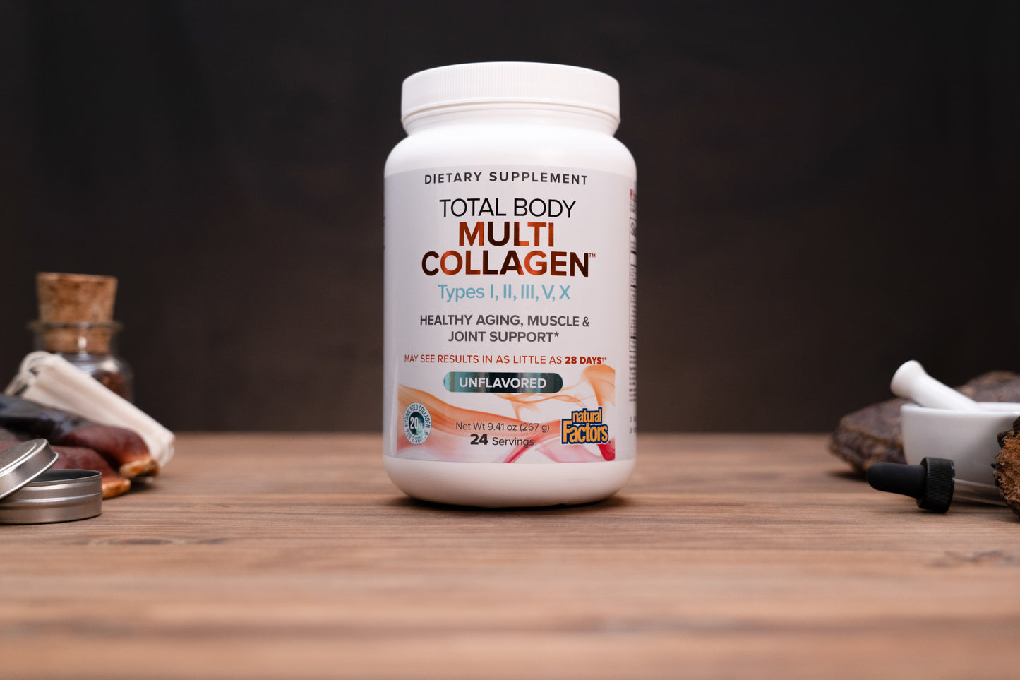 A white bottle of Total Body Multi Collagen dietary supplement standing on a wooden surface against a dark background, with small blurred props on both sides.