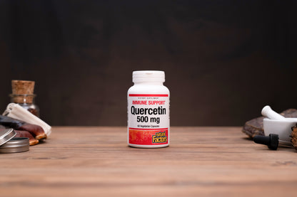 A white bottle of Quercetin 500 mg dietary supplement by Good Fakes, set on a wooden table with rustic herbal props in the background.