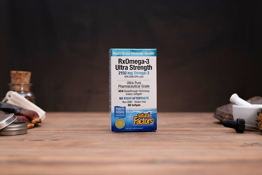 A box of Natural Factors RxOmega-3 Ultra Strength fish oil stands centered on a wooden tabletop with a dark blurred background. Small props are visible on both sides of the table.