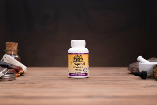 A bottle of Natural Ecos Ubiquinol 100 mg dietary supplement standing on a wooden surface against a dark background, with small mystical props visible on both sides.