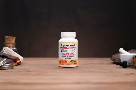 A bottle of Liposomal Vitamin C 1000 mg 300 mg dietary supplement, standing on a wooden surface with a dark, moody background and blurred herbal props on either side.