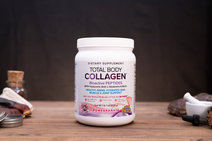 A white plastic bottle of Total Body Collagen dietary supplement with a white cap, set on a wooden surface with a dark, moody background and blurred herbal props.