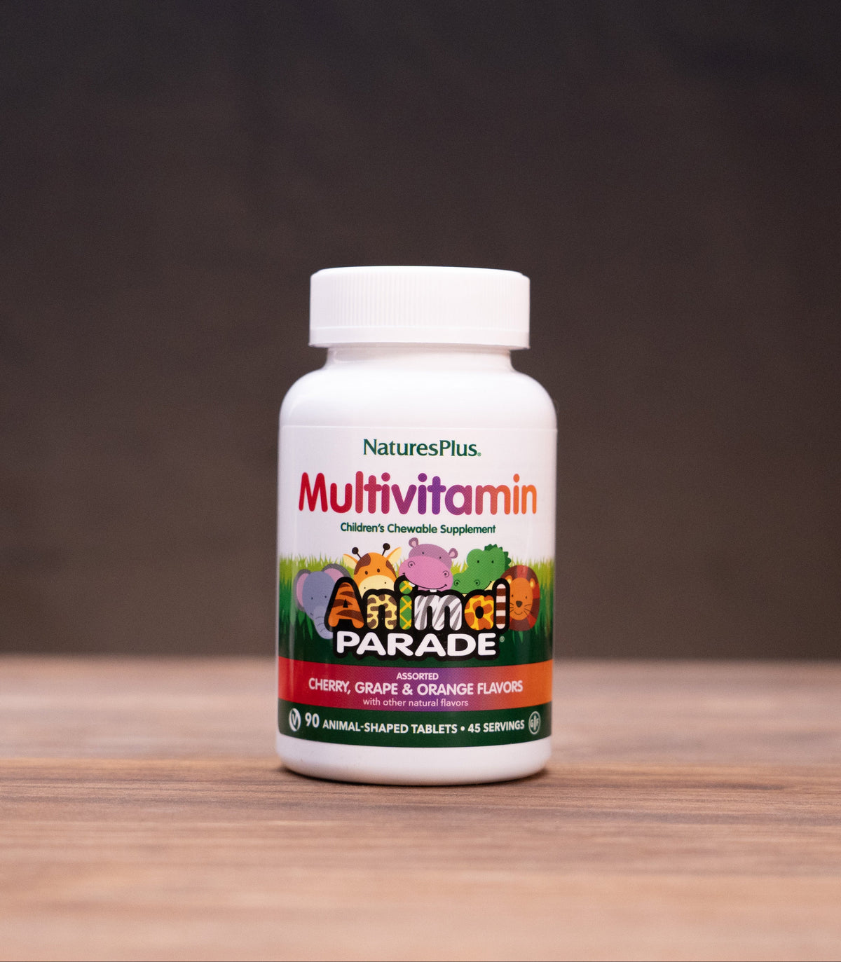 A bottle of Nature's Plus Multivitamin 'Animal Parade' dietary supplement, set on a wooden table with rustic props in the background.