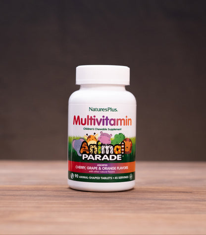 A bottle of Nature's Plus Multivitamin 'Animal Parade' dietary supplement, set on a wooden table with rustic props in the background.