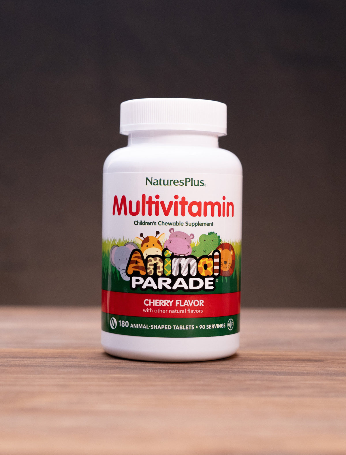 A bottle of Nature's Plus Animal Parade Multivitamin in cherry flavor, displayed on a wooden surface with rustic props in the background.