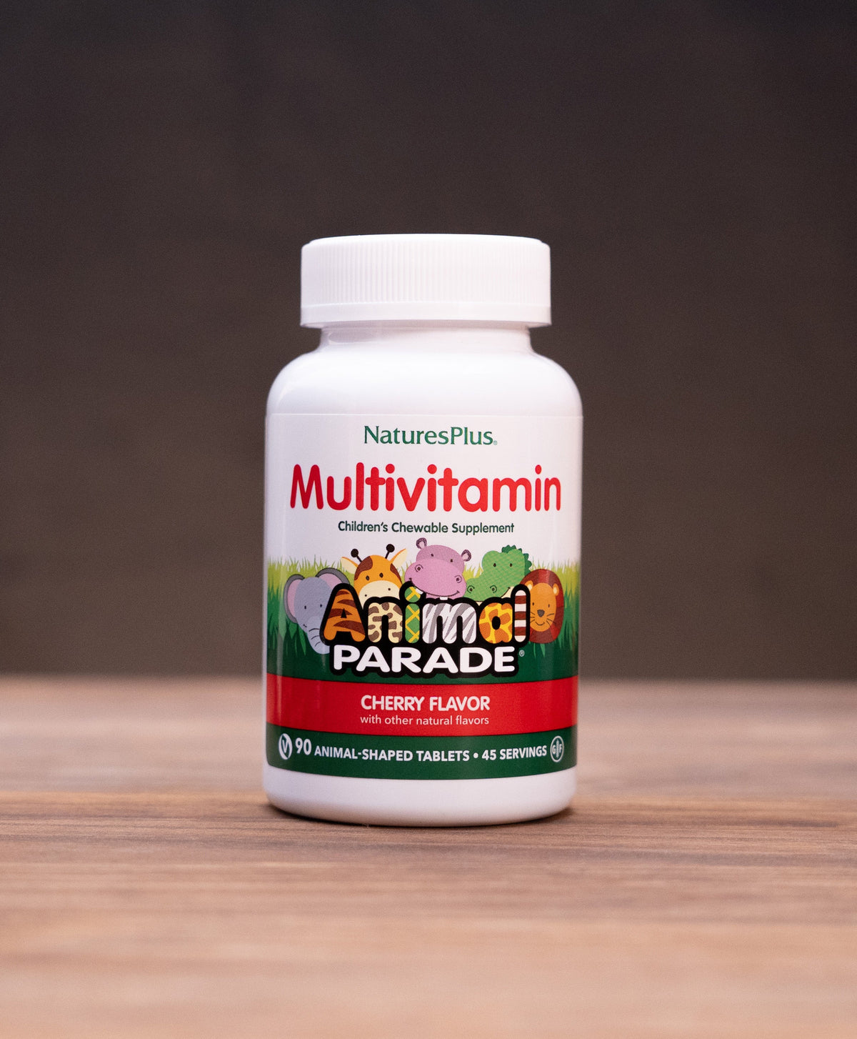 A bottle of Nature's Plus Multivitamin in Cherry Flavor, standing on a wooden table with rustic props like a mortar and pestle and dried herbs in the background.