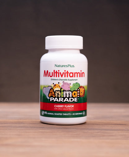 A bottle of Nature's Plus Multivitamin in Cherry Flavor, standing on a wooden table with rustic props like a mortar and pestle and dried herbs in the background.
