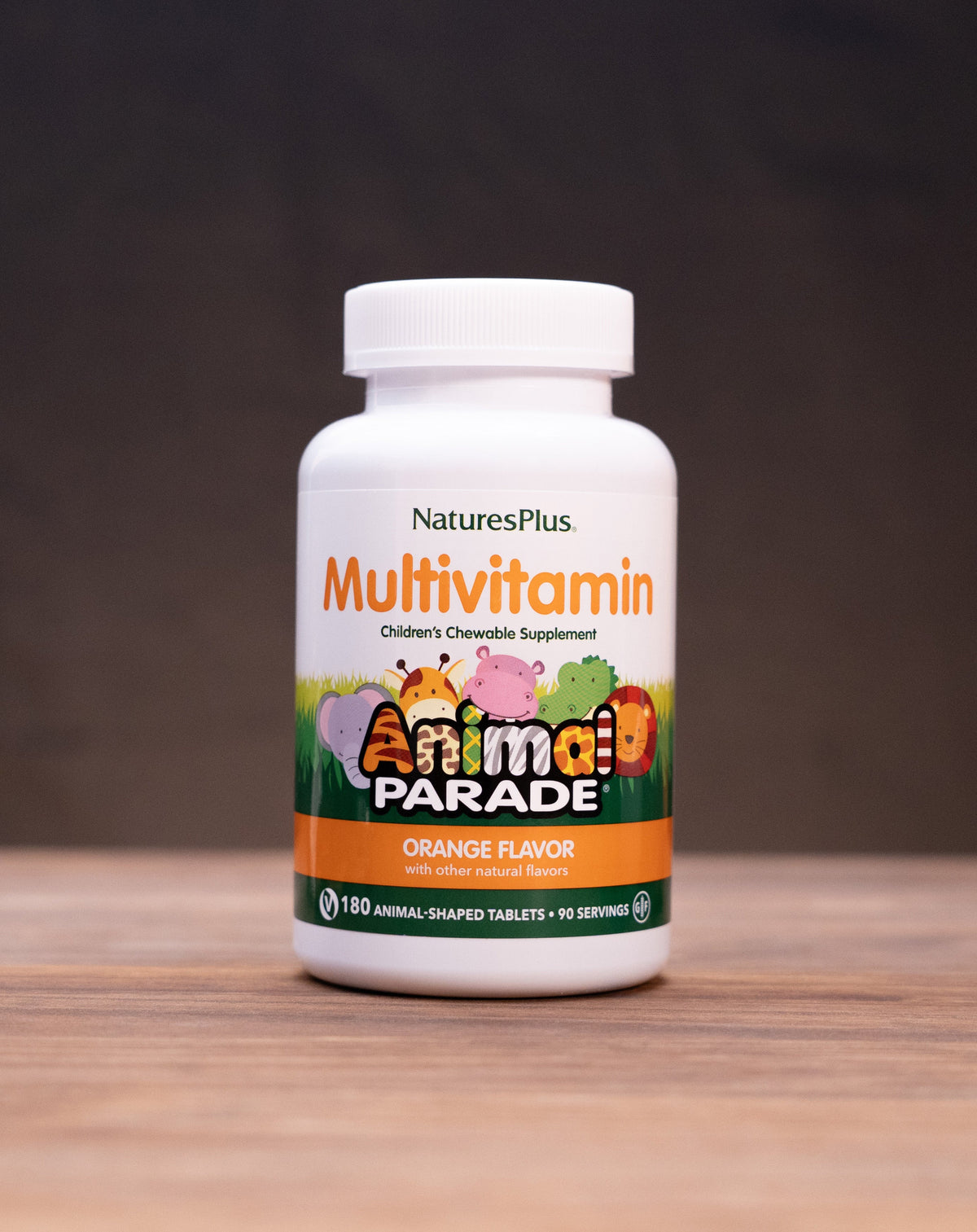A bottle of Nature's Plus Animal Parade Multivitamin in orange flavor, standing on a wooden surface with rustic props in the background.