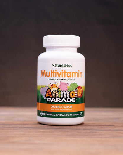 A bottle of Nature's Plus Animal Parade Multivitamin in orange flavor, standing on a wooden surface with rustic props in the background.