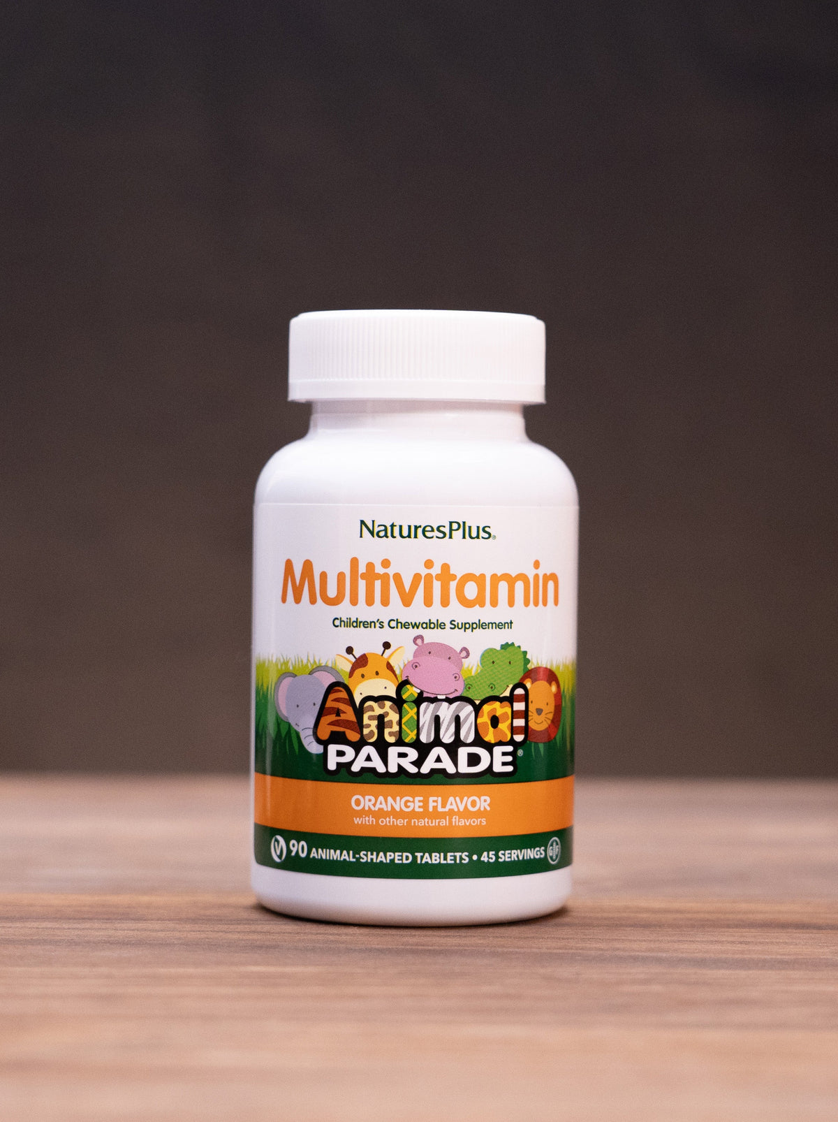 A bottle of Nature's Plus Multivitamin Orange Flavor, set on a wooden table with rustic props like a mortar and pestle, dried herbs, and a small jar in the background.