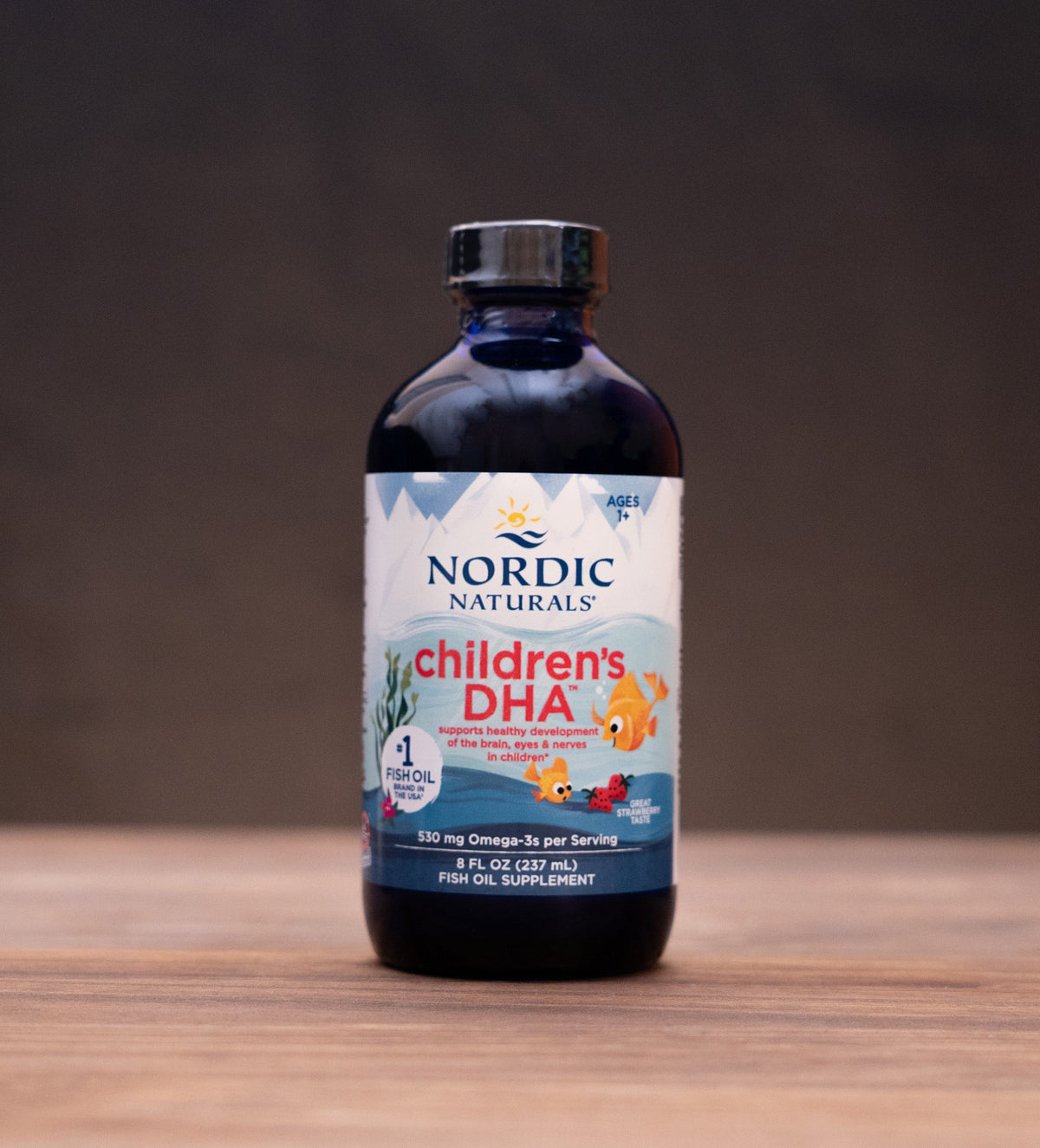 Nordic Naturals Children's DHA liquid supplement bottle on a wooden tabletop with rustic background props.