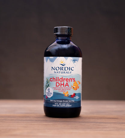 Nordic Naturals Children's DHA liquid supplement bottle on a wooden tabletop with rustic background props.