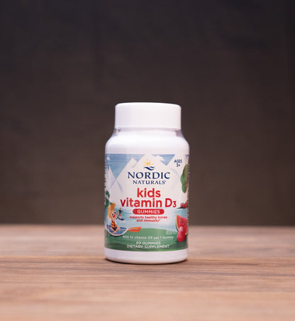 A bottle of Nordic Naturals Vitamin C dietary supplement standing on a wooden tabletop against a dark, blurred background.