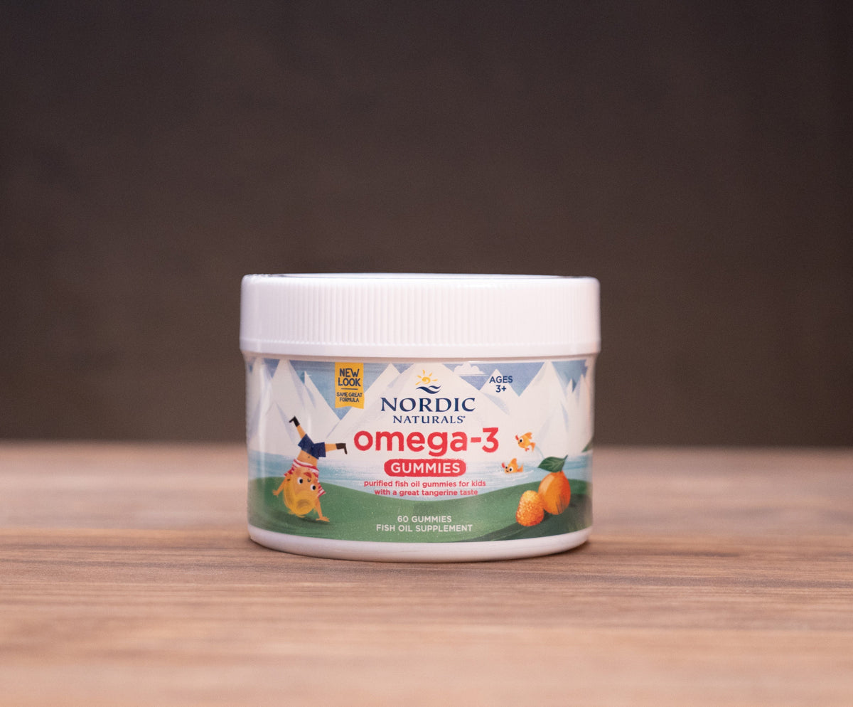 A jar of Norlin' Omega-3 fish oil capsules sits on a wooden table, surrounded by blurred natural ingredients and a dark background.