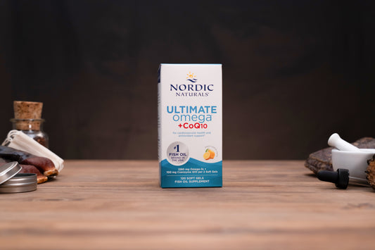 Nordic Naturals Ultimate Omega CoQ10 supplement box standing on a wooden tabletop with small props blurred in the background.