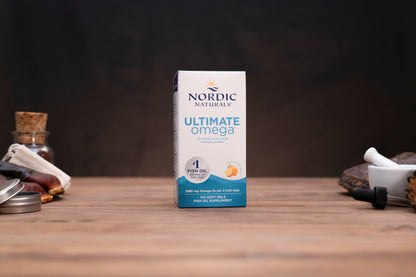 Nordic Naturals Ultimate Omega CoQ10 supplement box standing on a wooden tabletop with small props blurred in the background.