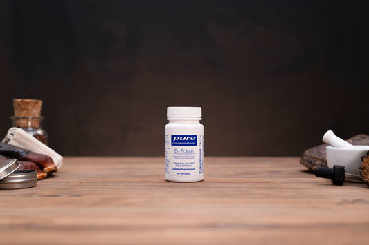 A white bottle of Pure Encapsulations Bi-Focus dietary supplement capsules, set on a rustic wooden table with mystical and herbal props in the background.