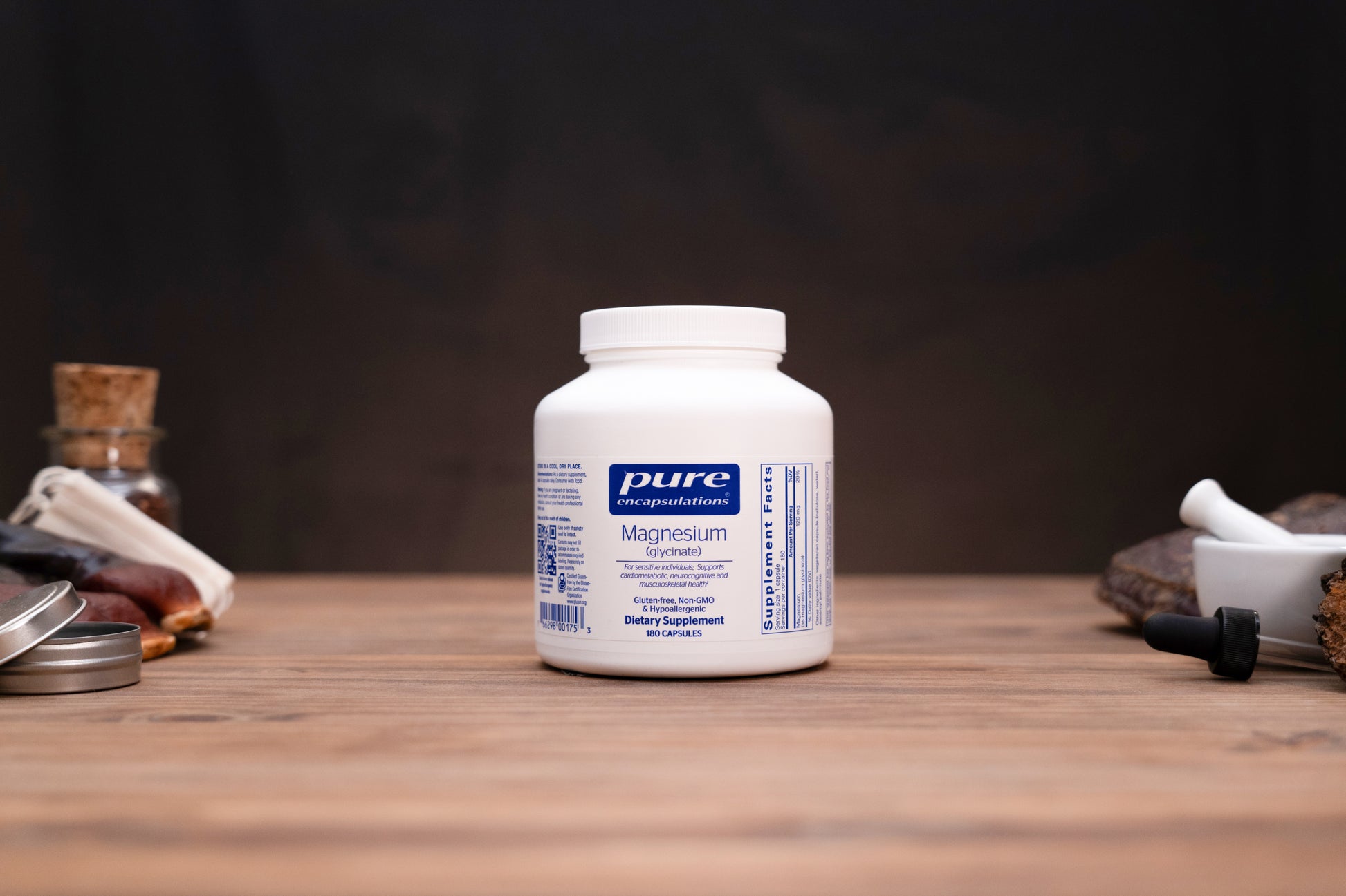 A white bottle of Pure Encapsulations Magnesium Glycinate dietary supplement, set on a rustic wooden table with blurred herbal props in the background.